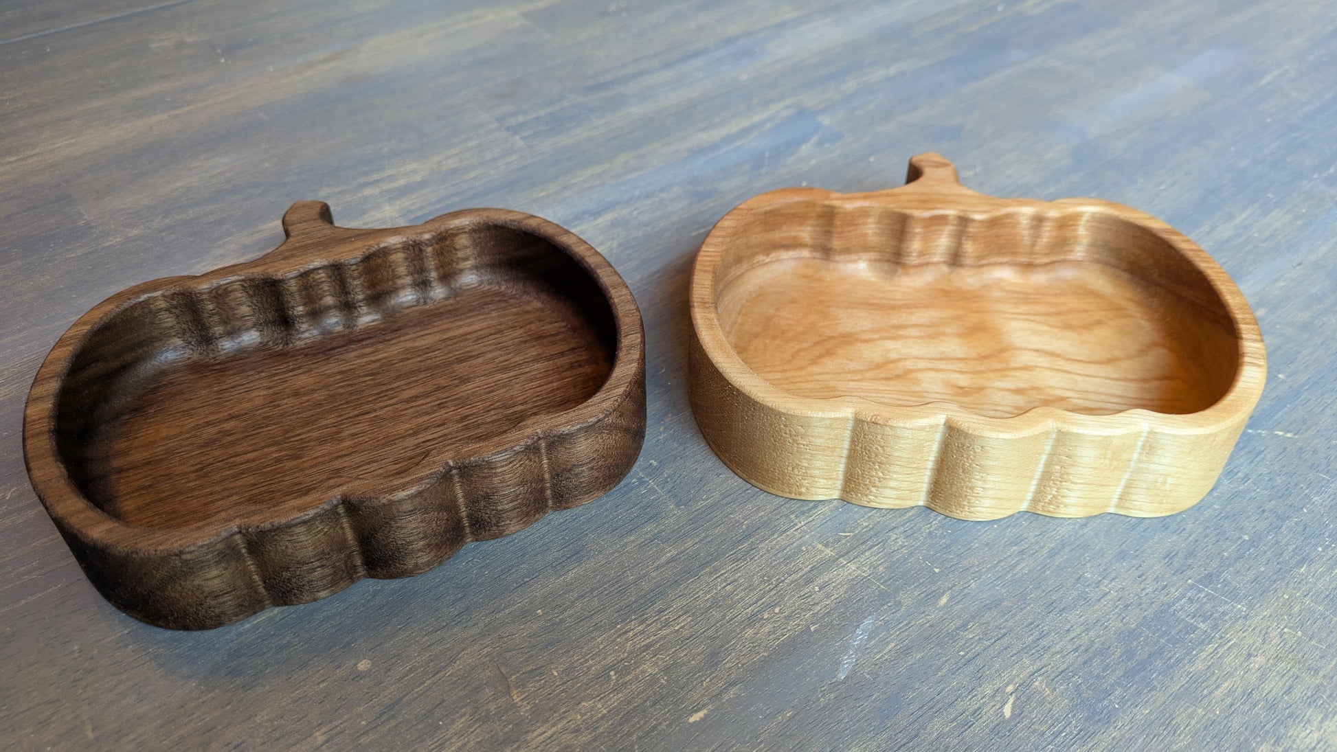 Two wooden pumpkin candy dishes, one dark brown and one light brown, on a table.